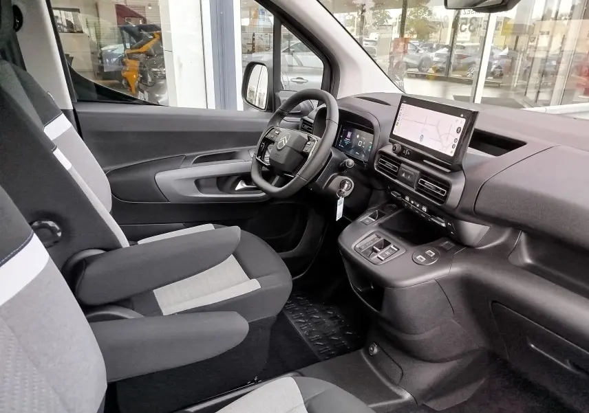 Intérieur du Citroën Berlingo 2025 vu côté conducteur, sièges gris et noir, tableau de bord avec écran tactile et volant multifonction.