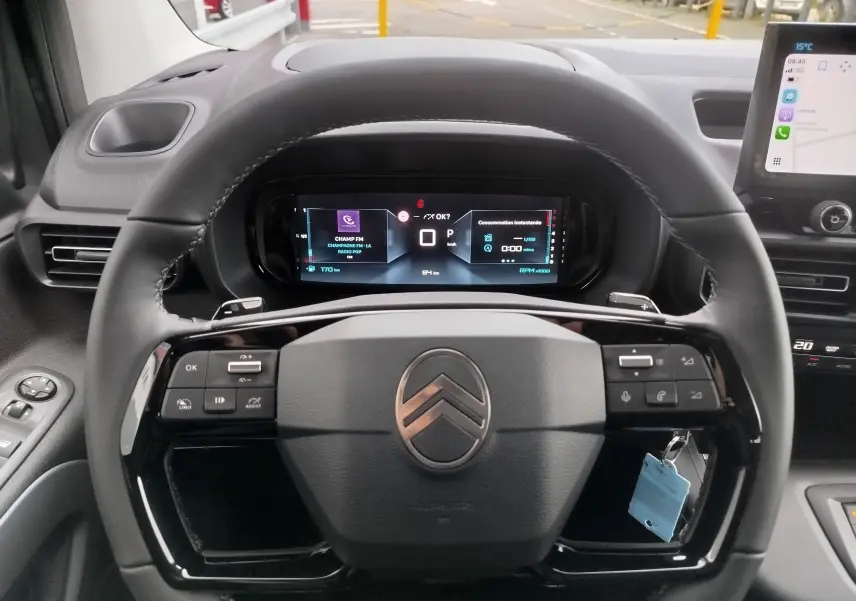 Vue rapprochée du volant noir de la Citroën Berlingo 2025 avec commandes intégrées et tableau de bord numérique allumé.