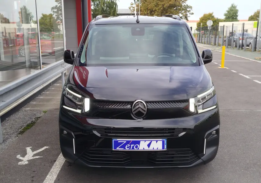 Vue avant d'un Citroën Berlingo noir Perla Nera avec feux LED allumés, stationné devant un bâtiment.