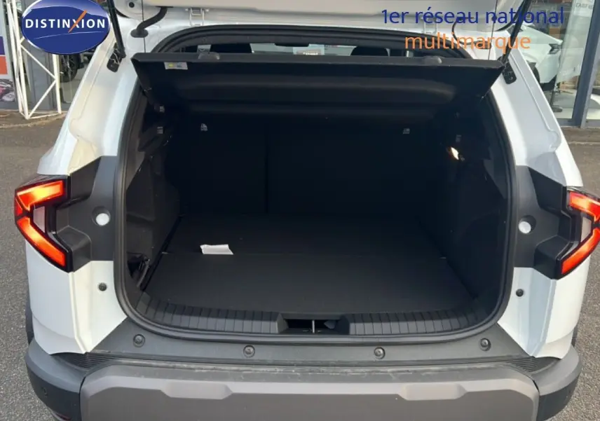 Vue arrière du Dacia Duster blanc glacier 2025 avec coffre ouvert et feux arrière allumés.