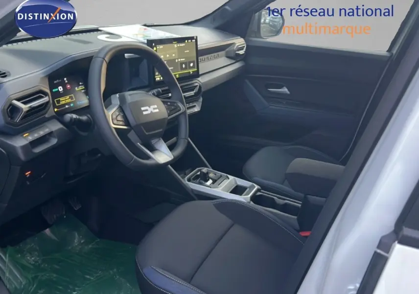 Vue intérieure côté conducteur du Dacia Duster blanc glacier 2025, avec tableau de bord numérique et écran tactile central.