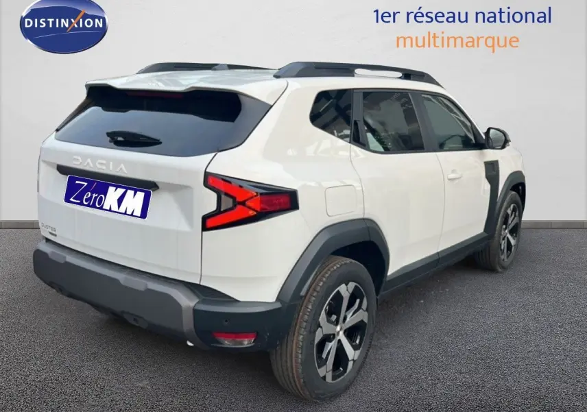 Vue 3/4 arrière droite du Dacia Duster blanc glacier 2025 avec jantes bi-ton et protections noires contrastantes.