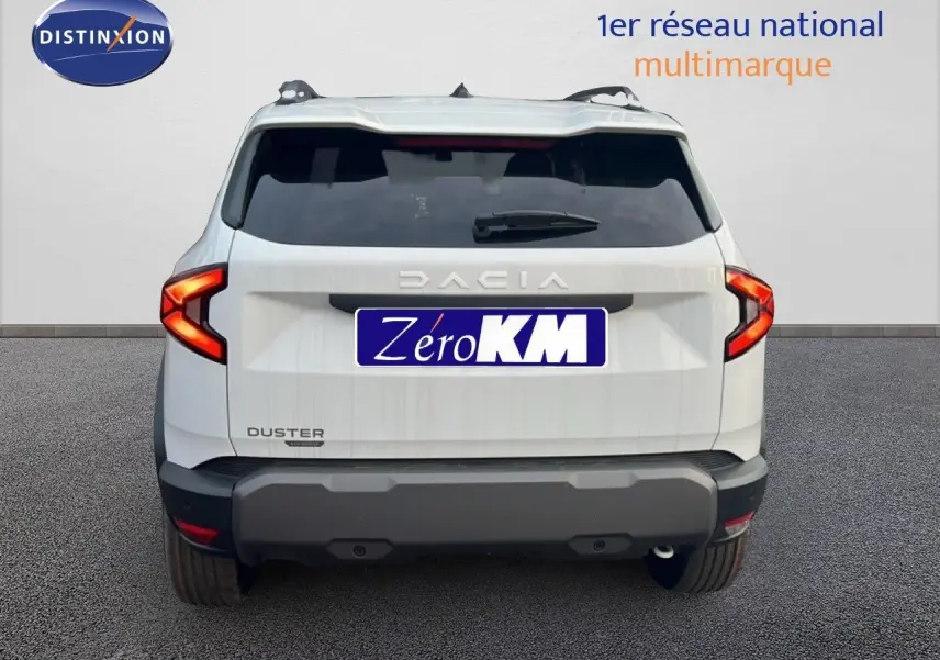 Vue arrière d'un Dacia Duster blanc glacier 2025 avec feux arrière allumés et plaque Zéro KM visible.
