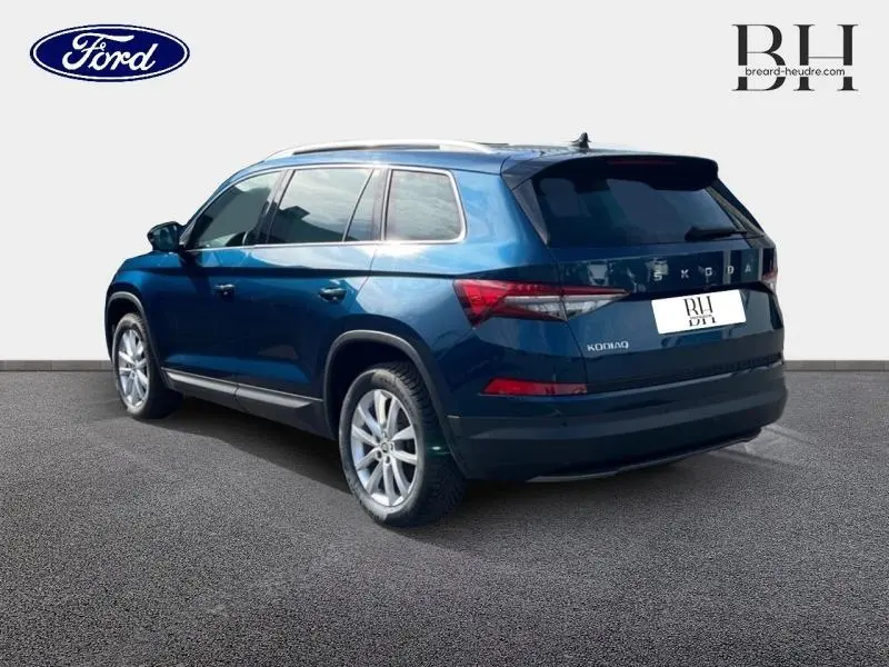 Vue 3/4 arrière droite d'un Skoda Kodiaq bleu lave métallisé avec jantes alu et barres de toit visibles.