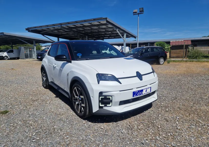Renault R5 E-TECH blanc nacré et noir en 3/4 avant droit sur parking avec plusieurs fourgons blancs en arrière-plan.