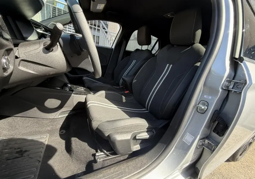 Vue intérieure côté conducteur de l’Opel Corsa 2025 gris aluminium, sièges noirs avec bandes blanches et volant visible.