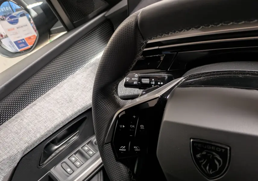 Vue intérieure rapprochée du volant noir perforé et des commandes surpiquées du Peugeot 3008 Hybrid 145 GT 2025.