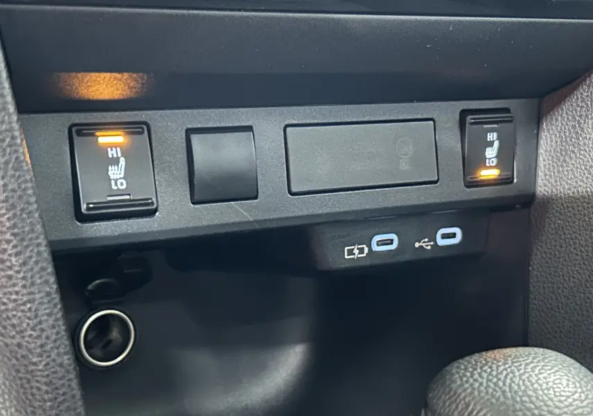Gros plan sur les commandes des sièges chauffants activés et les ports USB dans l’habitacle noir de la Toyota Yaris Cross gris minéral.