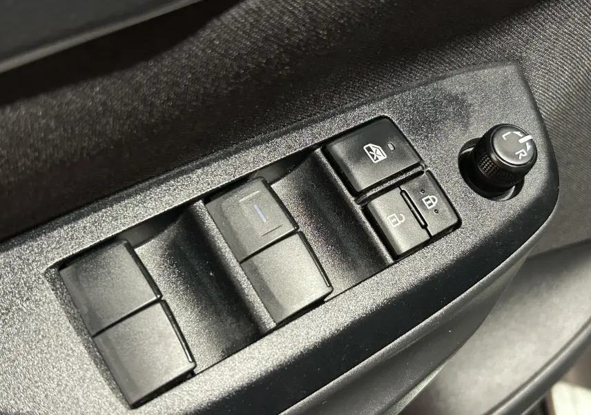 Gros plan sur les commandes de lève-vitres et réglage des rétroviseurs côté conducteur d'une Toyota Yaris Cross gris minéral.