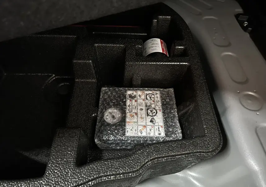 Gros plan sur le rangement intérieur du coffre d'une Toyota Yaris Cross gris minéral, montrant un kit de réparation pneu emballé.