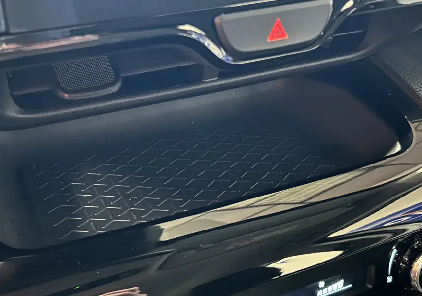Gros plan sur la console centrale noire brillante de la Toyota Yaris Cross 116h, avec bouton de signalisation rouge visible.