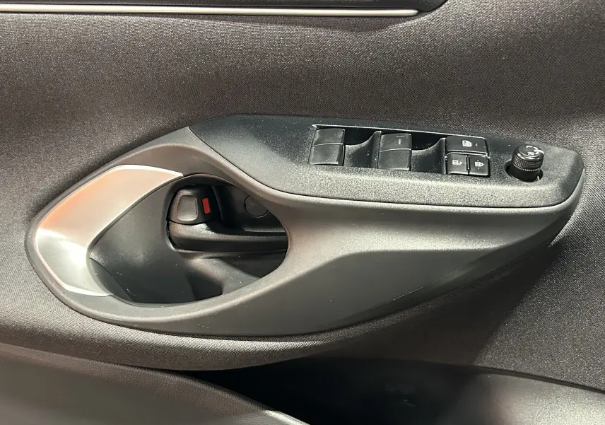 Gros plan sur la poignée intérieure et les commandes de lève-vitres côté gauche d’une Toyota Yaris Cross gris minéral.