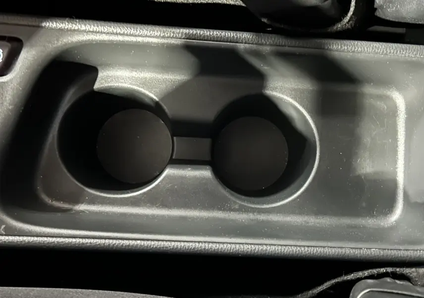 Gros plan sur les porte-gobelets centraux noirs de la Toyota Yaris Cross 116h Active MC24, intérieur sobre.