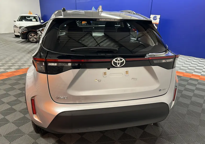 Vue arrière d'une Toyota Yaris Cross gris minéral 2025 avec feux arrière noirs et logo Toyota bien visible.