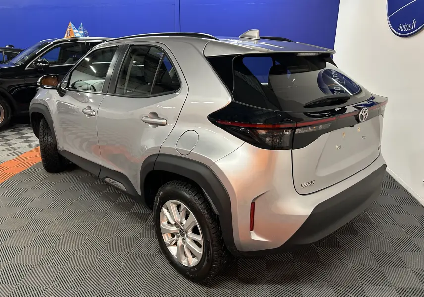 Vue 3/4 arrière droite d'une Toyota Yaris Cross gris minéral avec toit noir et jantes alliage en intérieur showroom.