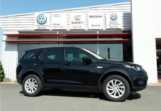 Profil côté gauche d'un Land Rover Discovery Sport Mark II noir, version TD4 150 SE A, stationné devant un garage multimarques.