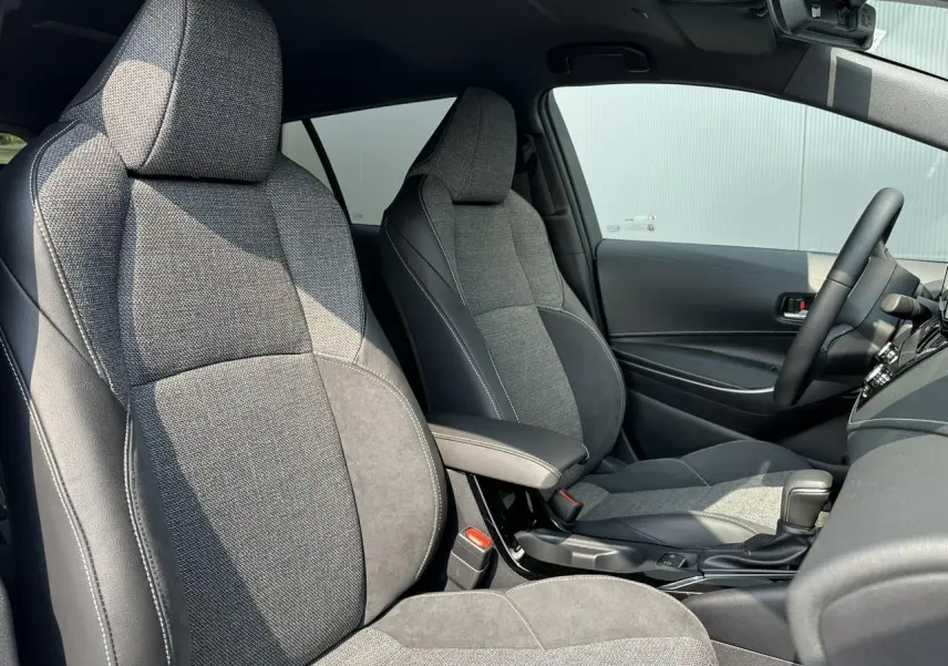 Intérieur avant de la Toyota Corolla Touring Sport 2025, sièges tissu gris et alcantara avec accoudoir central noir.