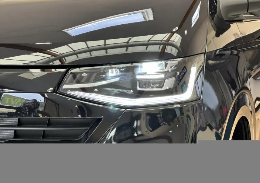 Gros plan sur le phare avant droit LED allumé du Volkswagen Transporter T7 ProCab noir Minuit, avec calandre partielle visible.