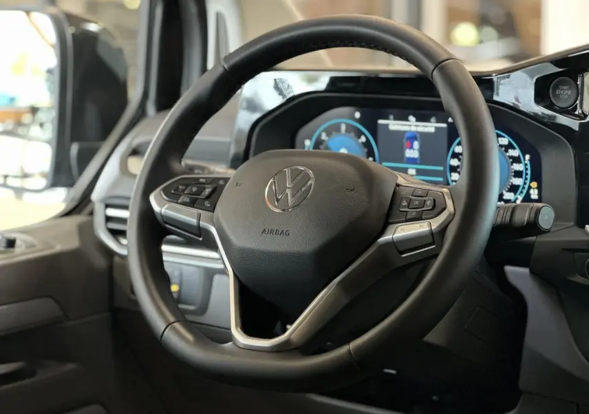 Vue rapprochée du volant multifonction noir du Volkswagen Transporter T7 avec tableau de bord digital en arrière-plan.