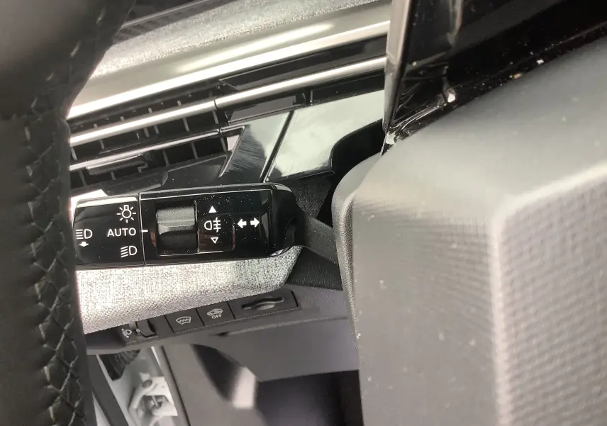 Gros plan sur la commande des feux et clignotants à gauche du volant dans l’habitacle du Peugeot 3008 blanc.