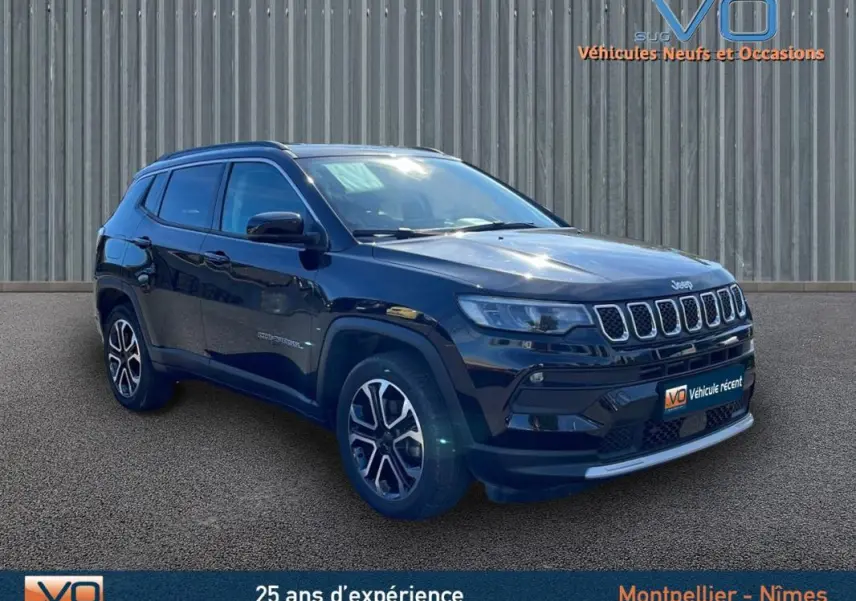 Jeep Compass noir en 3/4 avant droit, avec barres de toit et jantes 18 pouces visibles sur sol goudronné.