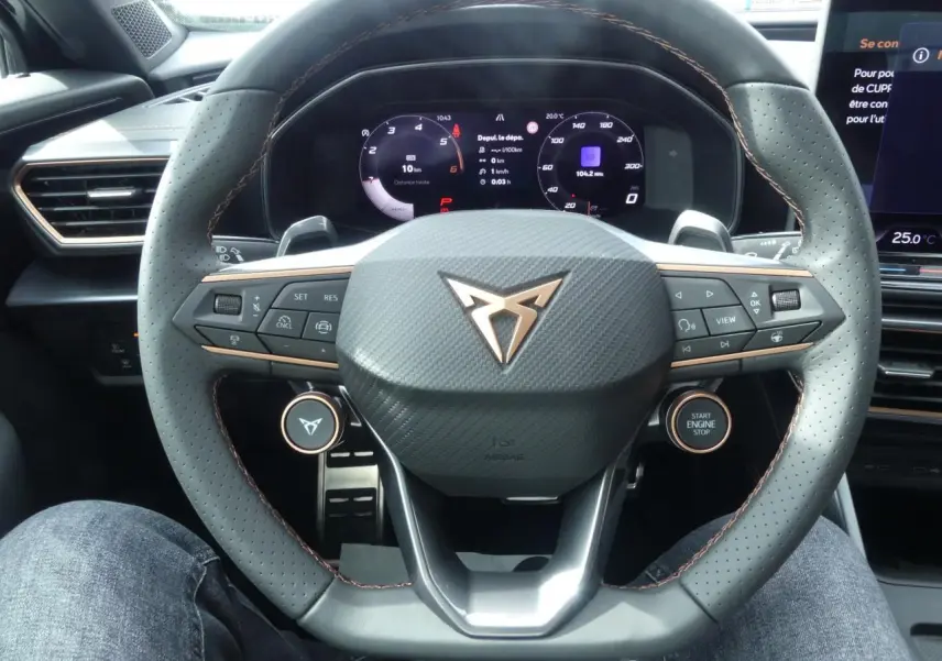 Vue rapprochée du volant perforé noir avec surpiqûres cuivrées et logo CUPRA sur tableau de bord digital.