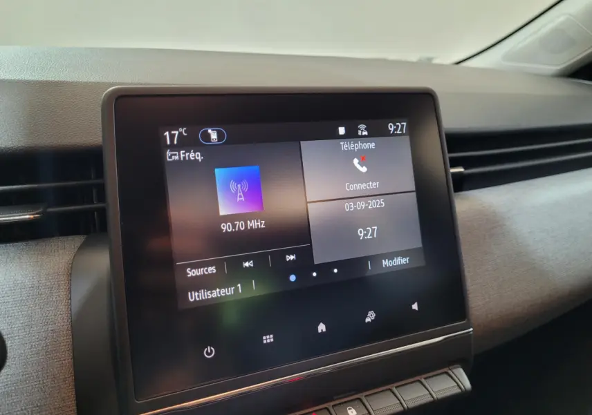 Écran tactile central de la Renault Clio gris foncé, affichant la radio et la connexion téléphone, vue intérieure rapprochée.