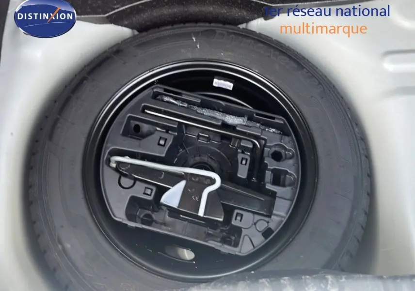 Vue rapprochée de la roue de secours noire et de son rangement dans le coffre d'une Citroën C3 blanche.