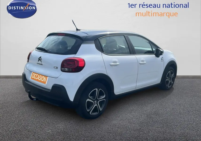 Citroën C3 blanc en 3/4 arrière droit avec toit noir et jantes distinctives, stationnée sur sol gris.