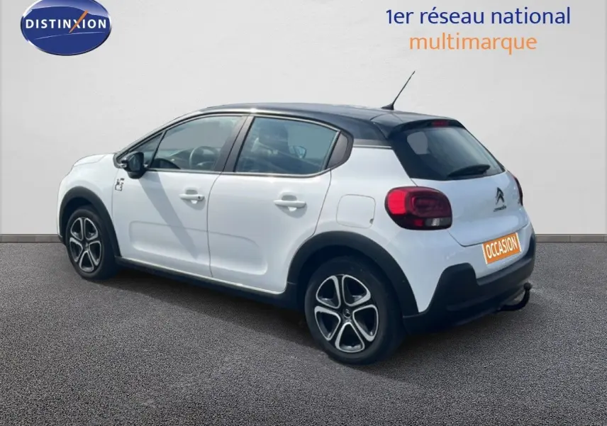 Vue 3/4 arrière droite d'une Citroën C3 blanche 2018 avec toit noir et jantes distinctives, en extérieur sur sol gris.