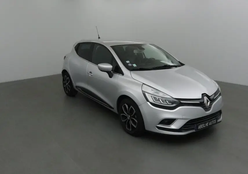 Renault Clio IV gris clair métal vue 3/4 avant droit, avec jantes biton et calandre distinctive Renault.