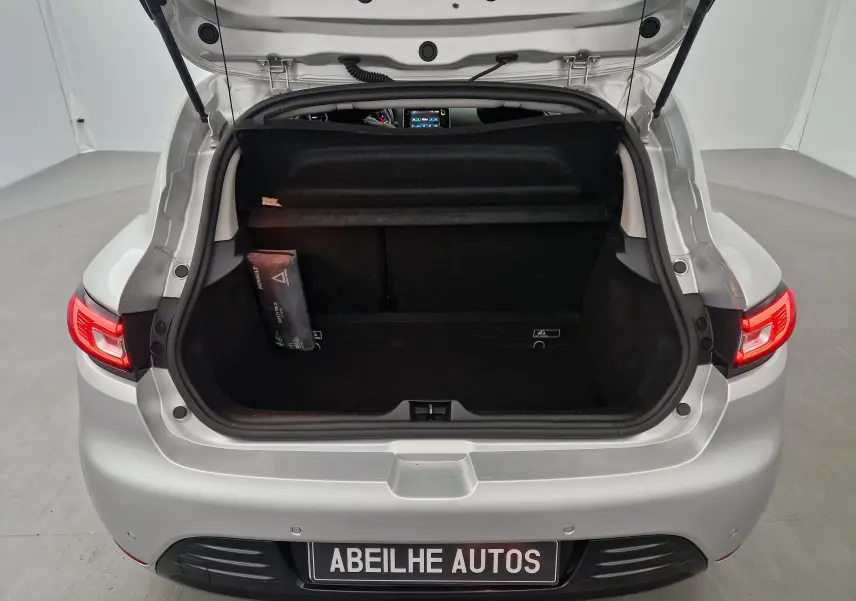Coffre ouvert vu de l'arrière d'une Renault Clio IV gris clair métallisé avec feux arrière allumés dans un studio.