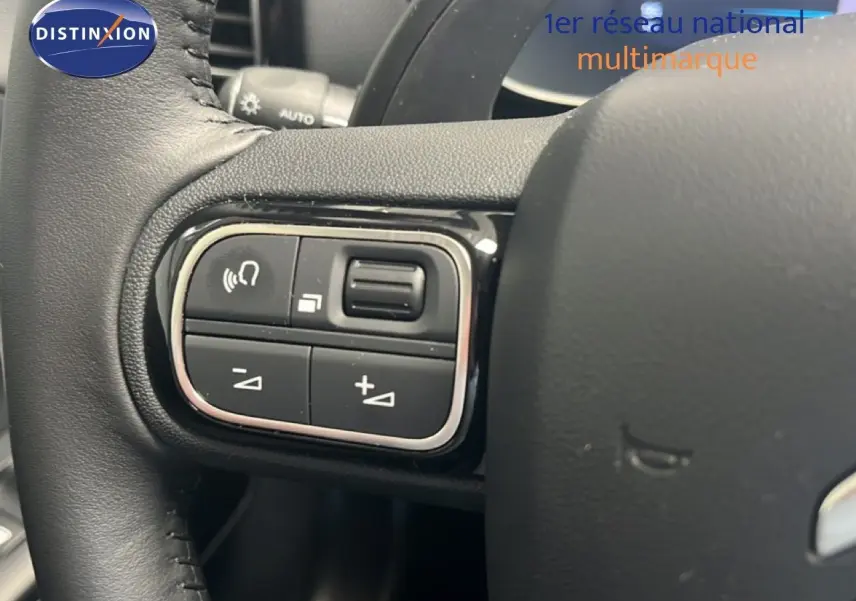 Gros plan sur les commandes gauche du volant noir du Citroën C5 Aircross hybride 2025, avec boutons de réglage audio.