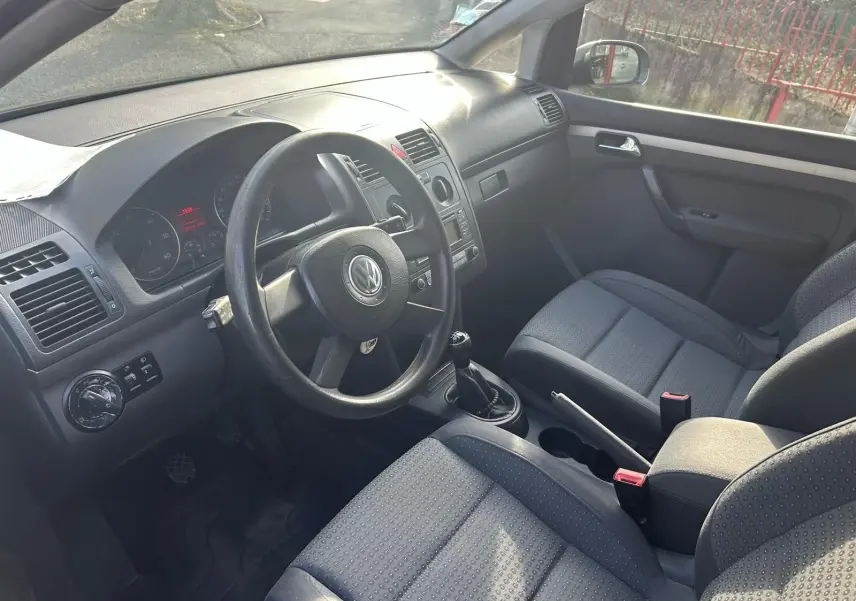 Intérieur du Volkswagen Touran 2004 vu côté conducteur, volant cuir, sièges tissu gris et boîte manuelle.