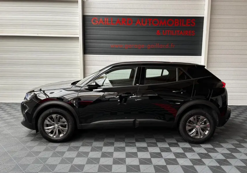 Profil côté gauche d'un Peugeot 2008 noir 2021 garé en intérieur sur sol à damier devant un mur blanc.