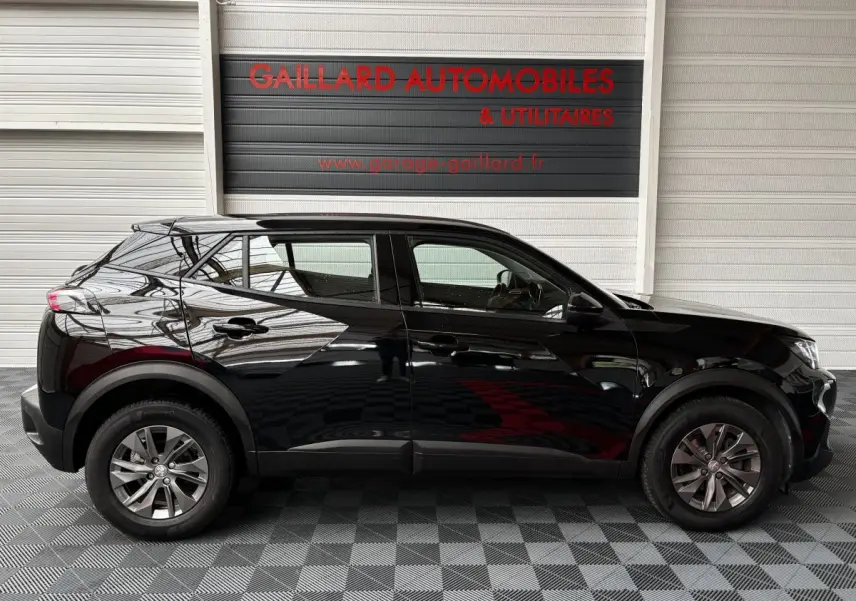 Profil côté gauche d'un Peugeot 2008 noir 2021 garé en intérieur avec reflets sur la carrosserie.