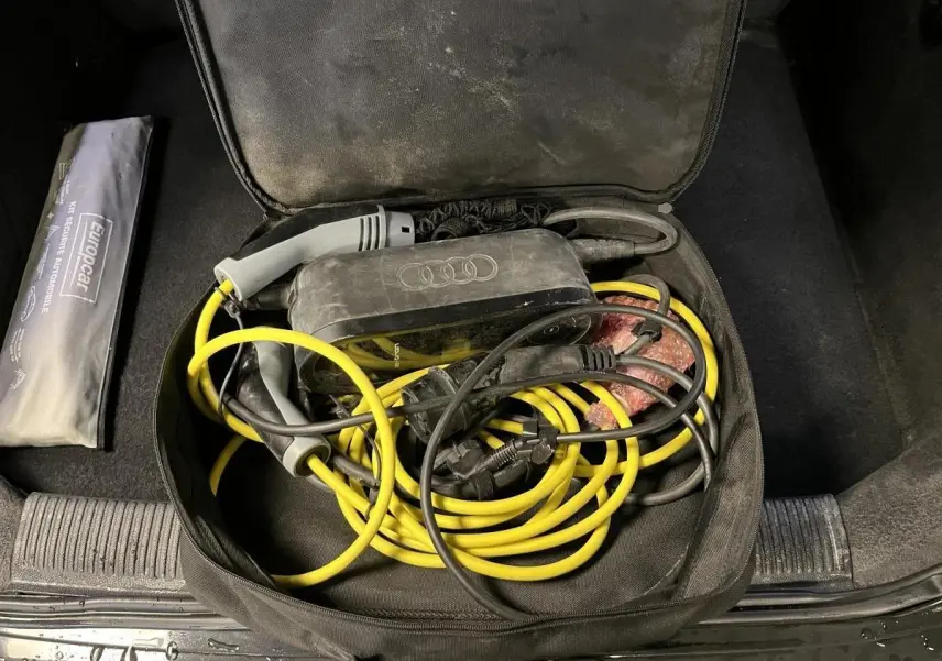 Coffre ouvert d'une Audi A3 noire avec câble de recharge hybride jaune et noir rangé dans un sac noir.