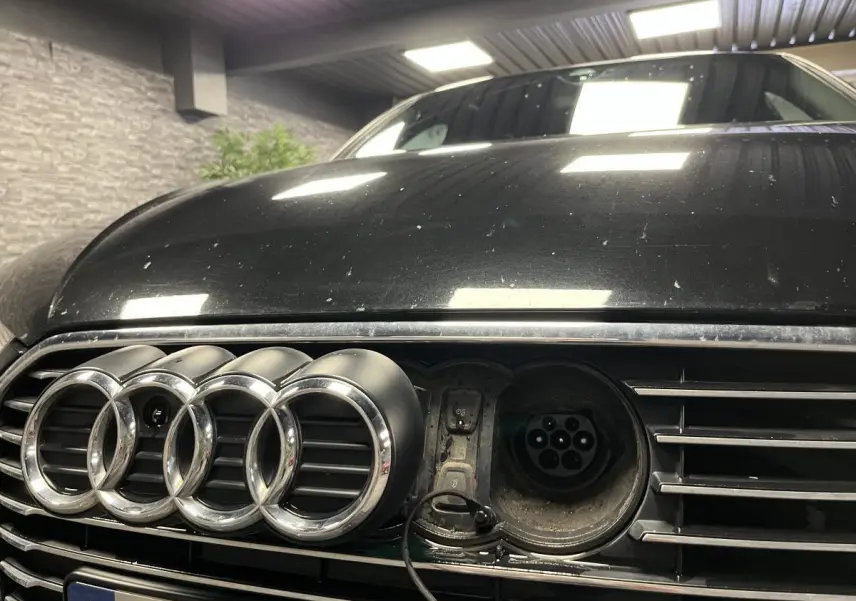 Gros plan sur la calandre avant noire d'une Audi A3 1.4 TFSI e-tron S line avec prise de recharge visible à droite des anneaux.