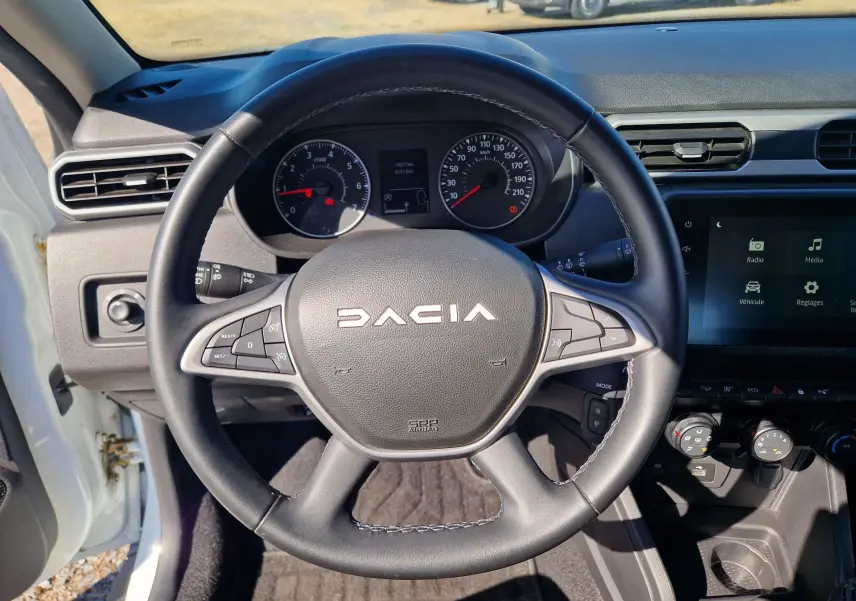 Vue intérieure centrée sur le volant noir du Dacia Duster 2024 avec tableau de bord et écran tactile visibles.