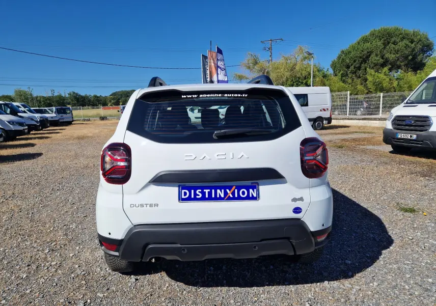 Vue arrière d'un Dacia Duster blanc 4x4 2024, avec logo et plaque Distinxion visible sur un terrain extérieur.