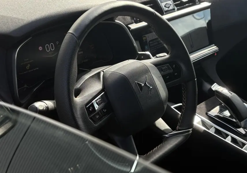 Vue rapprochée du volant en cuir noir perforé avec surpiqûres Carmin et Or du DS7 2024, tableau de bord et écran tactile visibles.
