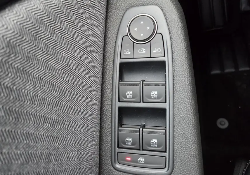 Gros plan sur les commandes des vitres électriques et rétroviseurs dans l'habitacle gris mélangé de la Renault Clio V 2025.