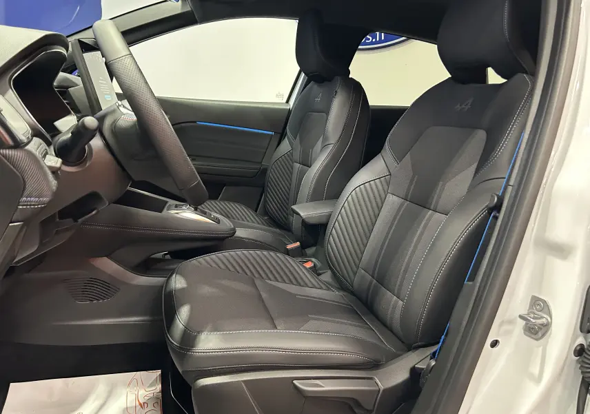 Vue intérieure côté conducteur du Renault Captur blanc nacré 2026, sièges noirs avec surpiqûres bleues et volant chauffant.