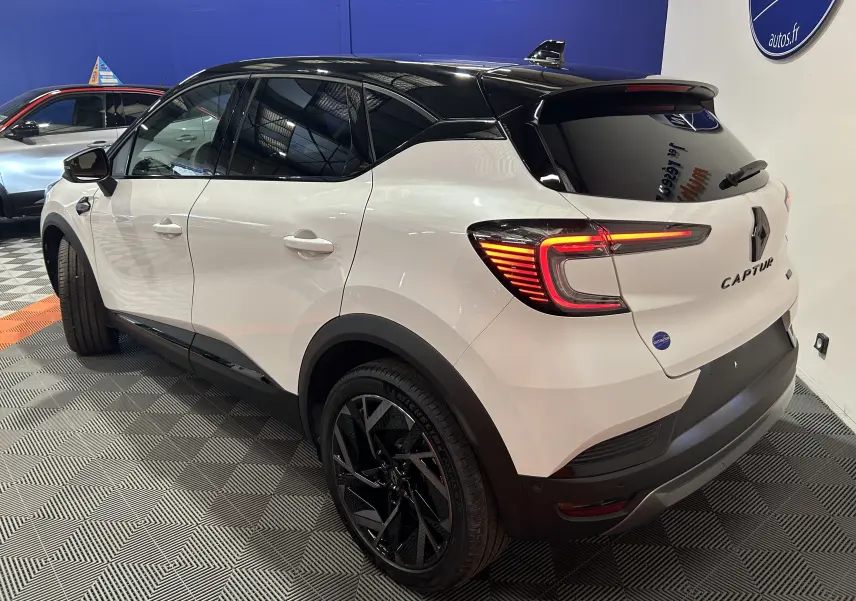 Vue 3/4 arrière droite du Renault Captur blanc nacré avec toit noir et feux arrière allumés en intérieur showroom.
