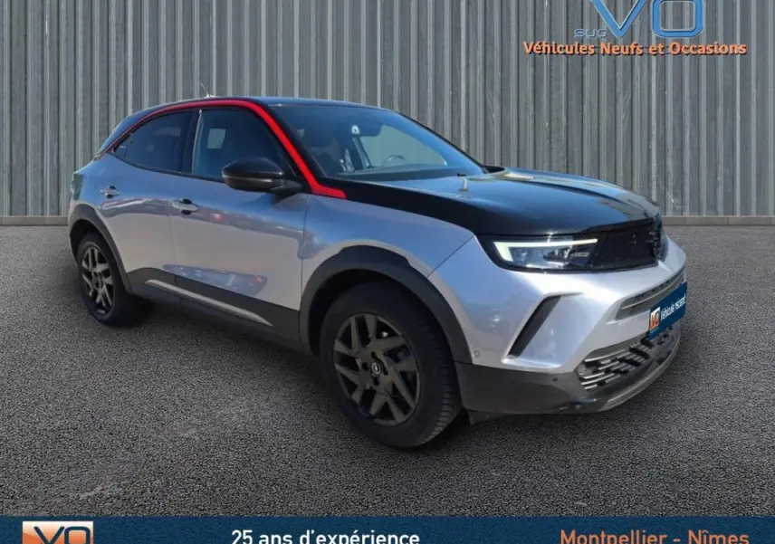 Opel Mokka gris clair vue 3/4 avant droit avec capot noir et jantes alliage 18 pouces sur fond neutre.