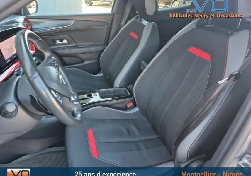 Vue intérieure côté conducteur de l'Opel Mokka gris clair 2022, sièges noirs avec surpiqûres rouges et volant cuir.