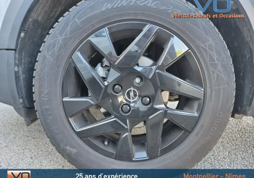 Gros plan sur la jante alliage noire 18 pouces avec logo Opel du côté gauche d’un Opel Mokka gris clair 2022.