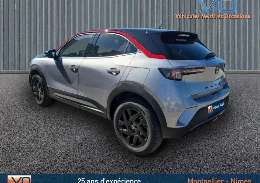 Opel Mokka gris clair vue 3/4 arrière droit, jantes alliage noires 18 pouces et toit noir avec liseré rouge.