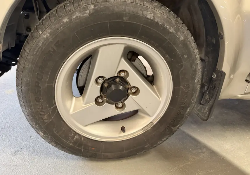 Gros plan sur la jante alu grise et le pneu d'un Suzuki Jimny Cabriolet 2005, côté avant droit.