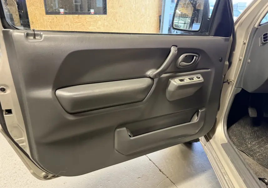 Vue intérieure de la porte avant droite grise du Suzuki Jimny Cabriolet 2005 avec commandes électriques des vitres.